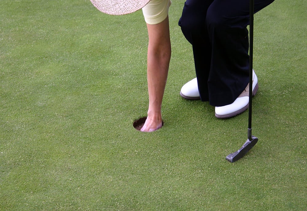 female golfer picking up the ball from the hole